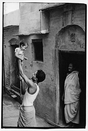 Man holding small boy in the air while a woman looks on from doorway.
