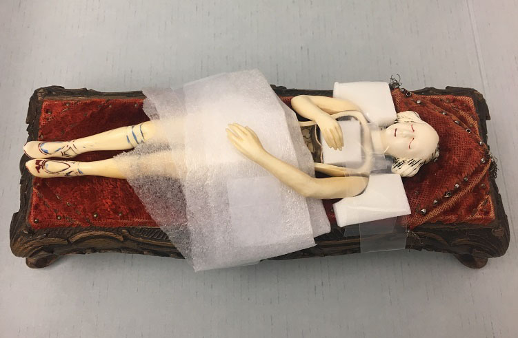 Ivory manikin on small wooden bed