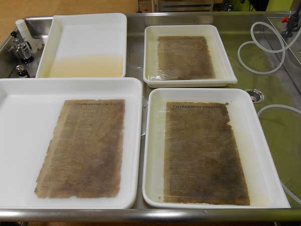 Aqueous treatment to remove discoloration and degradation products.  The upper left tray shows the extent of discoloration removed from a page in its first bath.
