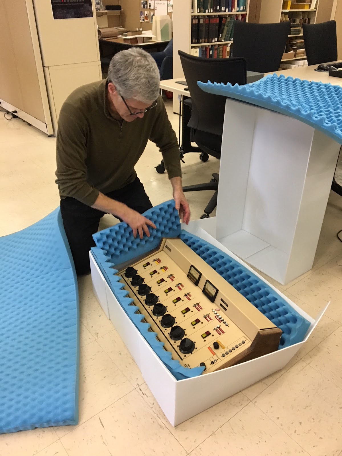 Archivist kneeling over a large box with the soundboard inside.