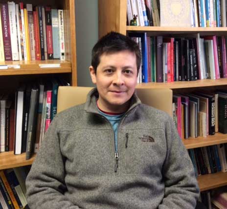 Photo of Dr. Raul Necochea in his office, with bookshelves behind him.