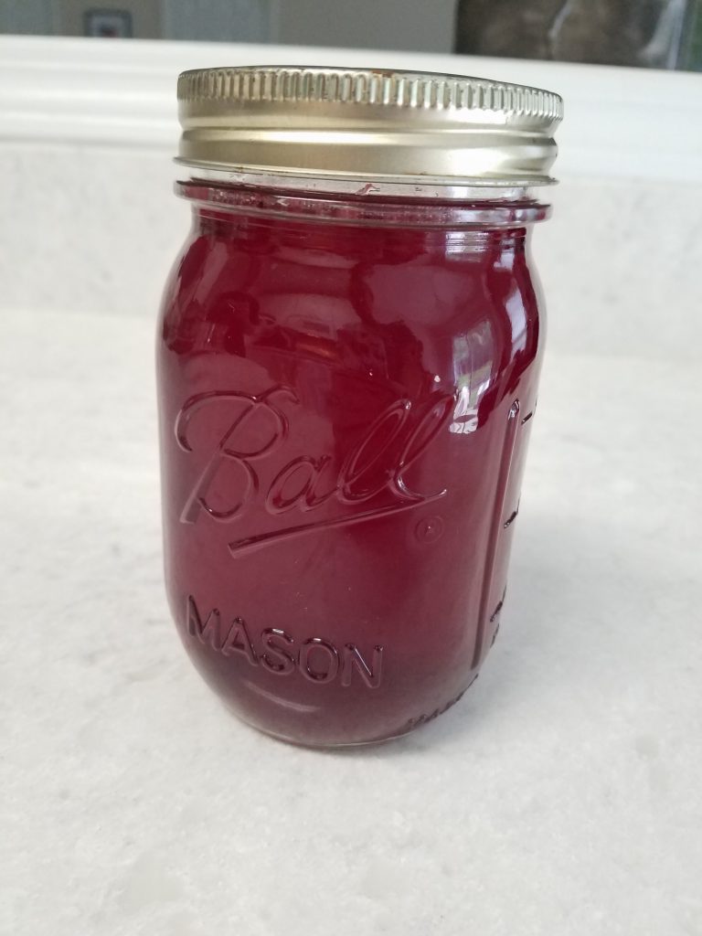 photograph of raspberry shrub in a glass mason jar. the liquid in the jar is a dark red. 