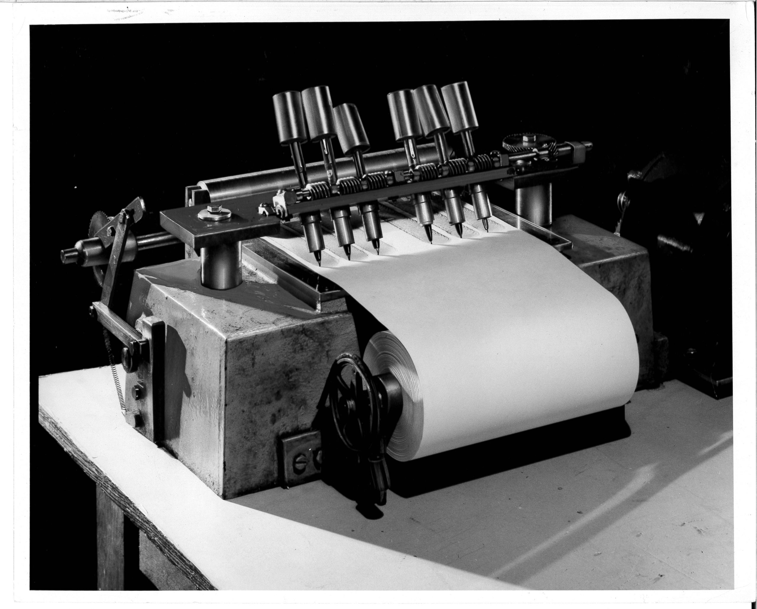 Image showing pen testing equipment with six pens writing on a white sheet of paper.