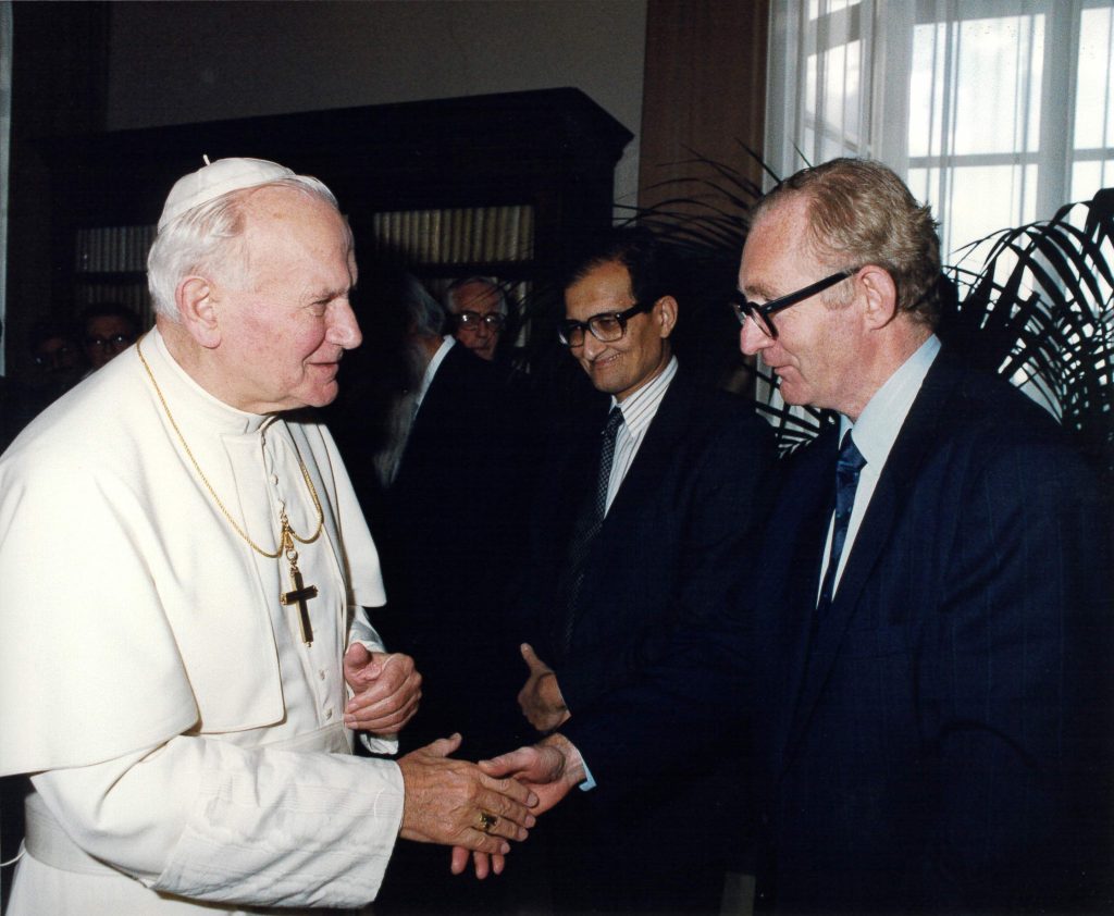 Atkinson shakes hands with Pope John Paul II. Amartya Sen is in line to Atkinson's right in the background.