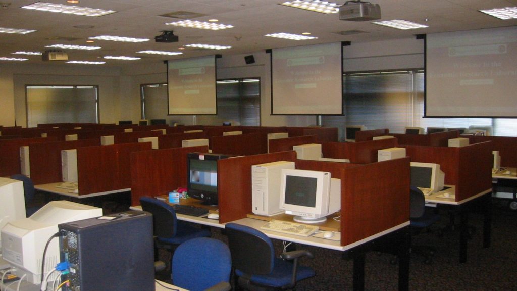 A university computer lab with dividers separating each desktop computer. Each computer has a CRT monitor and large tower.