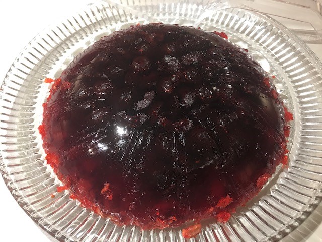 Dark red, circular jello mold with cherries visible inside on a round glass plate. 