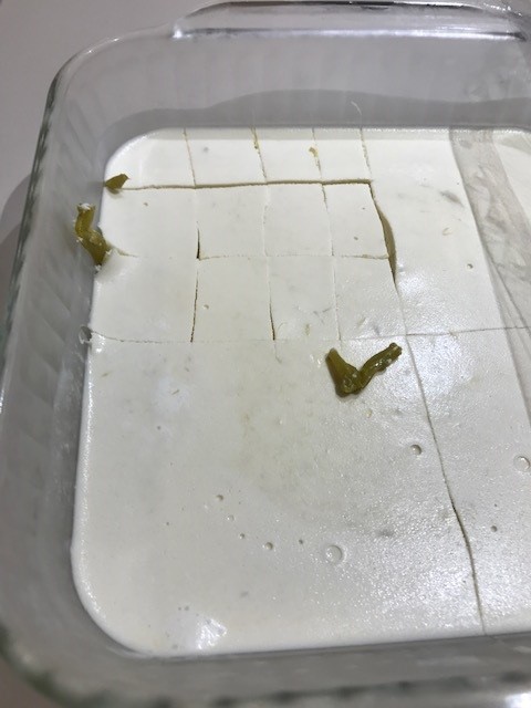 Thick white asparagus mold in a  square glass container. The mold is cut into small pieces with a few stalks of green asparagus showing between the slices. 