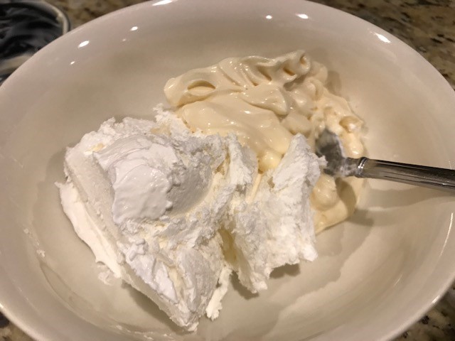 A white bowl containing a scoop of white Cool Whip next to a scoop of off-white mayonnaise. 