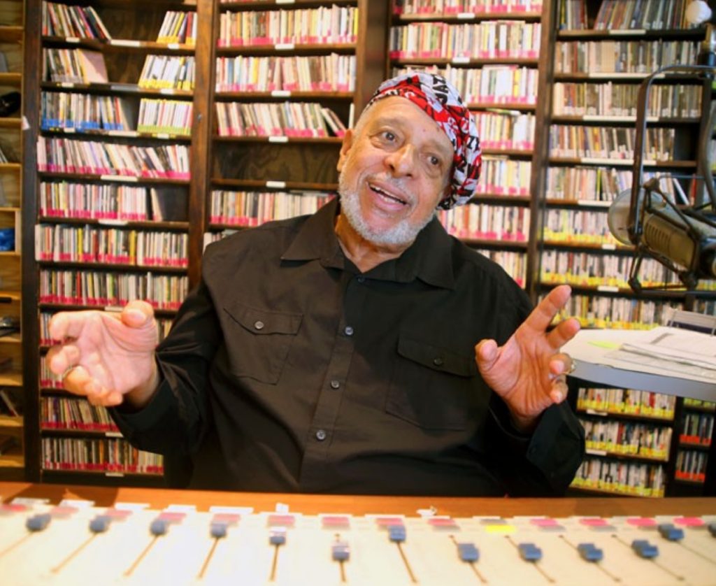 Image of Michael Gourrier sitting in front a piano with shelves of CDs in the background