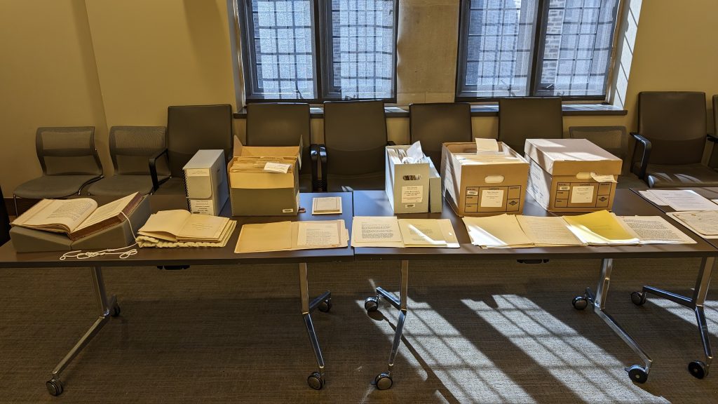 A table with several archival boxes and documents laid out on top of it.