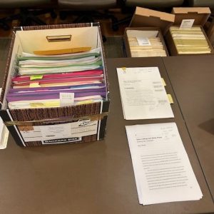 An archival box with folders and papers of different colors, as well as a couple of documents, on a table.