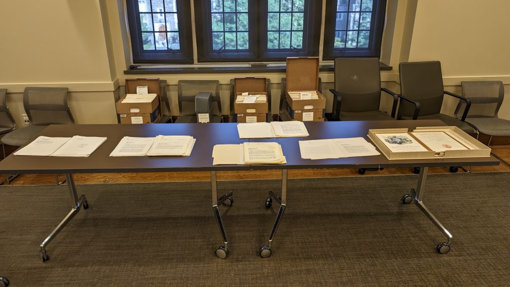 A table with several archival boxes and documents laid out on top of it.