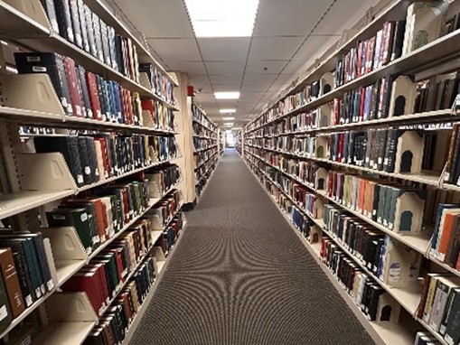 A photo looking down the aisle between two long library shelves full of books. 