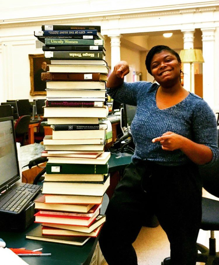Tall stack of books on desk with woman