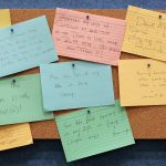 Multicolored index cards pinned to a corkboard with handwritten messages on them.