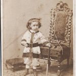 19th century photo of a 4 year old boy standing by a chair