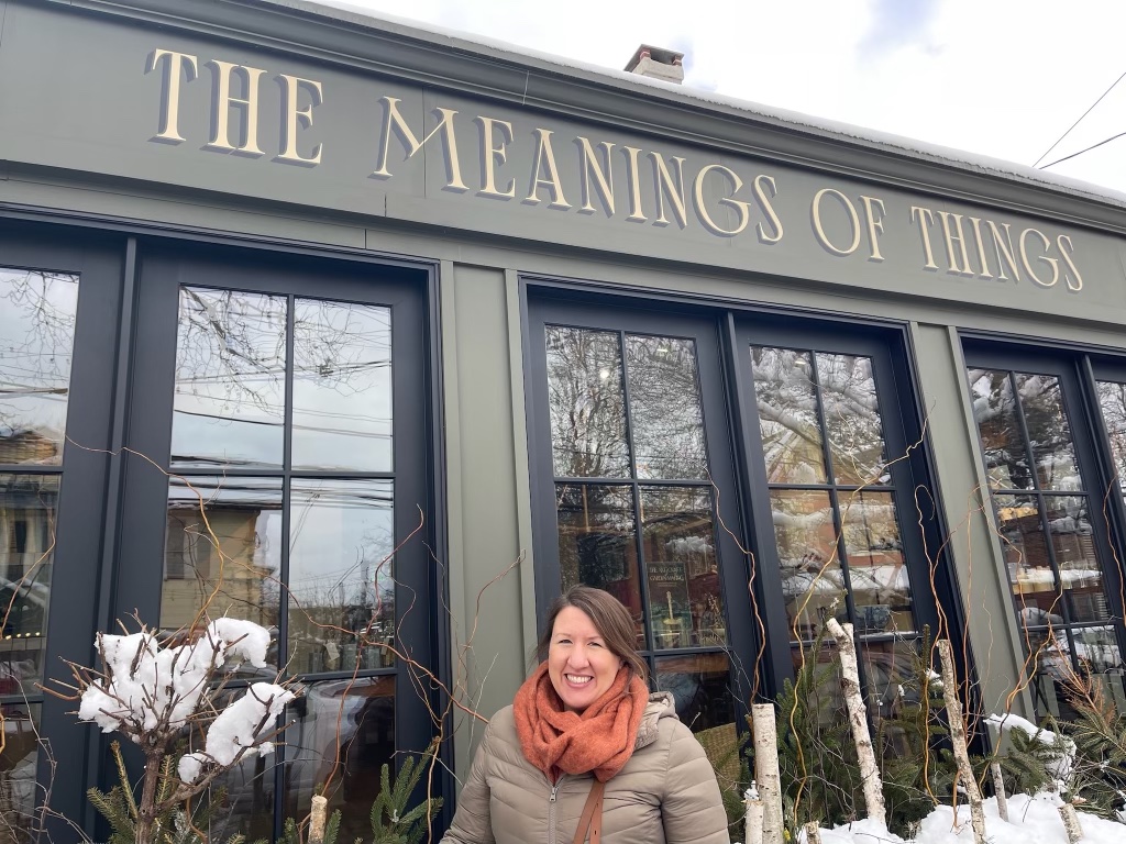 Woman in red scarf standing in front of a store called "The Meanings of Things"